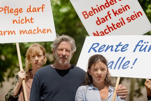 Demo für soziale Gerechtigkeit Gruppe von Menschen verschiedenen Geschlechts und Alters, mit und ohne Behinderung, demonstrieren. Auf den Demopappen steht "Pflege darf nicht arm machen", "Behinderung darf kein Nachteil sein" und "Rente für alle"